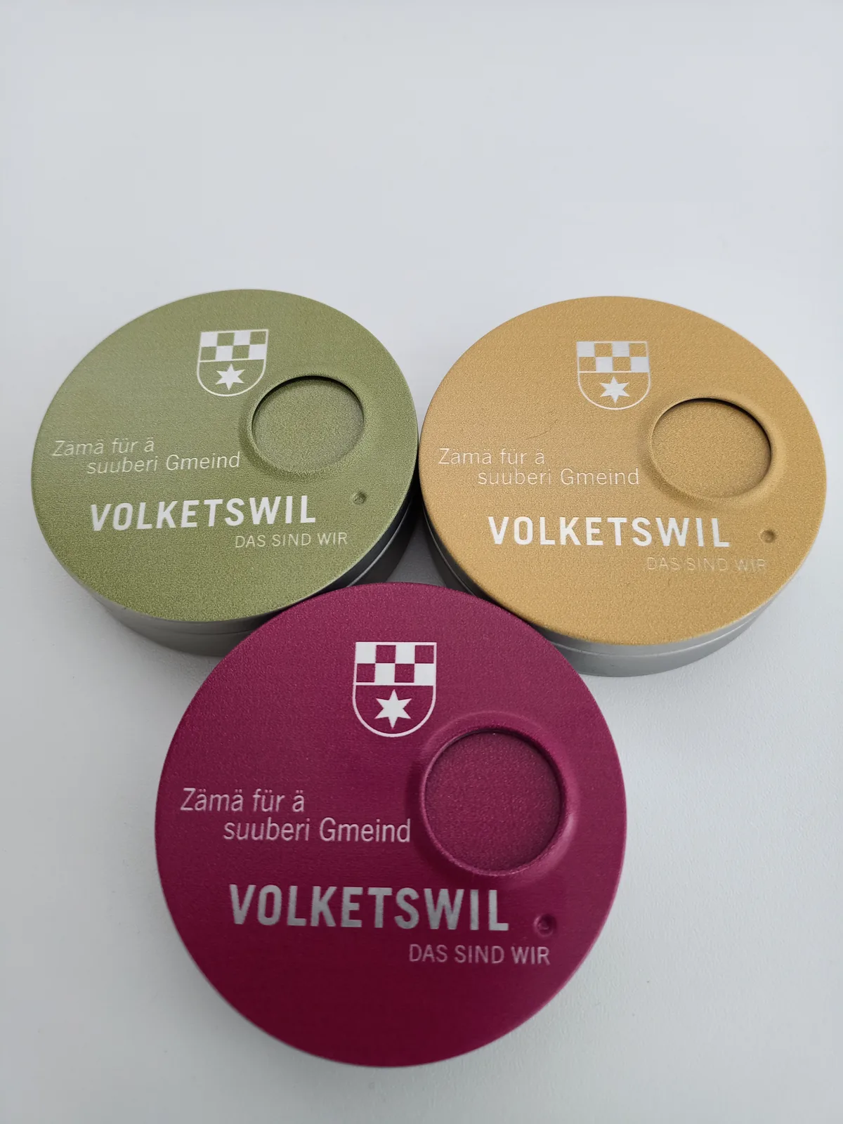 Man sieht drei kreisrunde, farbige portable Aschenbecher.